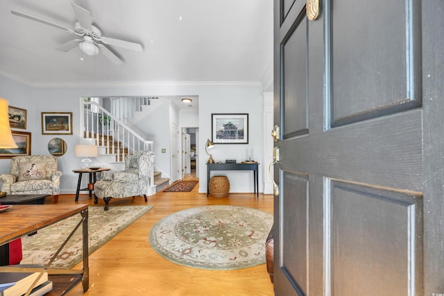 foyer with stairway, ornamental molding, wood finished floors, a ceiling fan, and baseboards