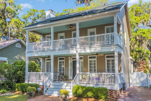 view of front of home with ceiling fan, a balcony, covered porch, and a chimney