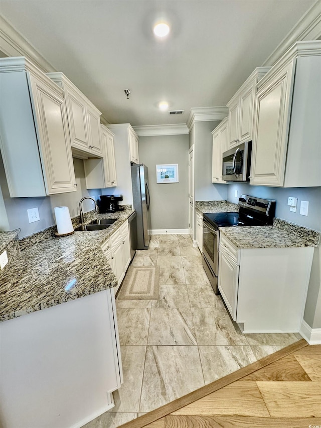 kitchen featuring stainless steel appliances, a sink, crown molding, stone counters, and baseboards