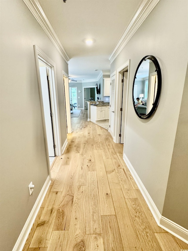 hall featuring crown molding, light wood-style flooring, and baseboards