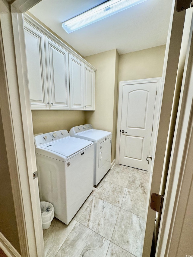 laundry area featuring washer and clothes dryer, cabinet space, and light marble finish floors