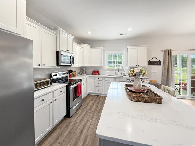 kitchen featuring appliances with stainless steel finishes, a sink, a center island, backsplash, and white cabinets