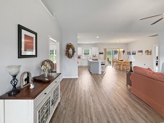 living area featuring a chandelier, wood finished floors, a ceiling fan, lofted ceiling, and baseboards