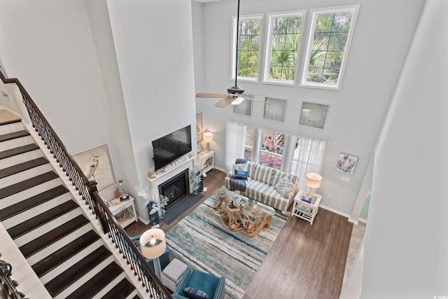living area featuring healthy amount of natural light, stairs, a high ceiling, a fireplace with flush hearth, and a ceiling fan