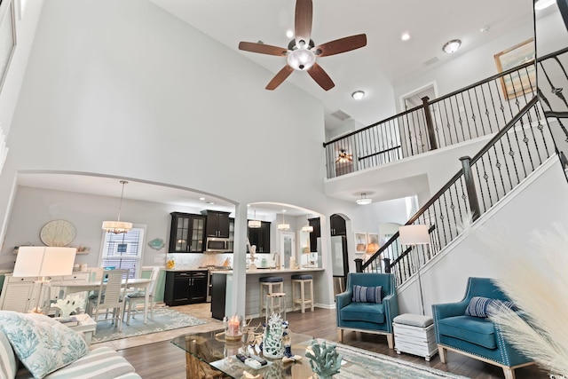 living area with arched walkways, a ceiling fan, wood finished floors, a high ceiling, and recessed lighting