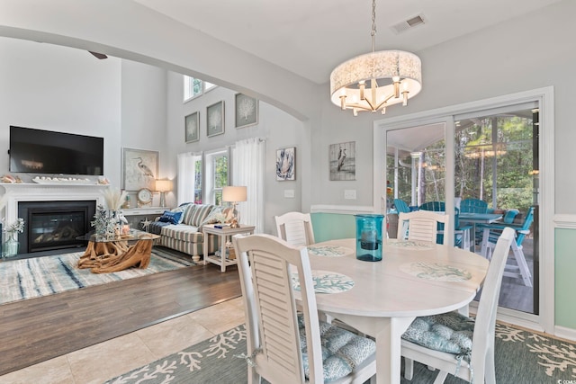 dining space with a chandelier, tile patterned flooring, arched walkways, and a glass covered fireplace