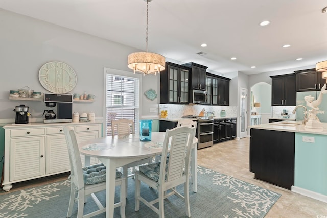 kitchen with appliances with stainless steel finishes, tasteful backsplash, a chandelier, light countertops, and glass insert cabinets