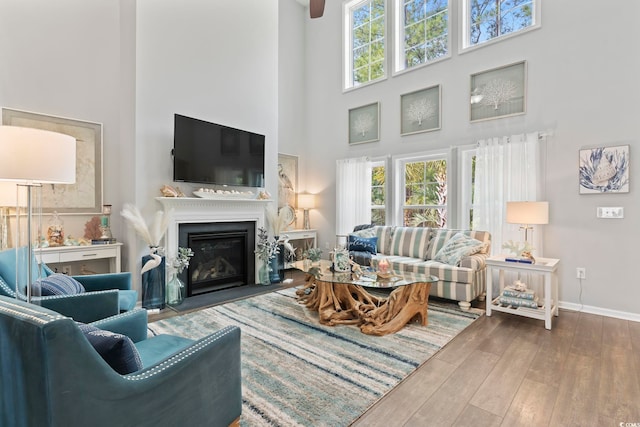 living area featuring a high ceiling, wood finished floors, baseboards, and a glass covered fireplace