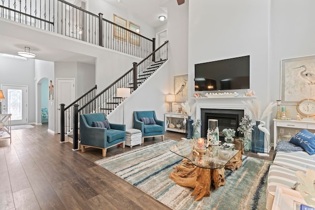 living room with a towering ceiling, stairway, wood-type flooring, arched walkways, and a glass covered fireplace