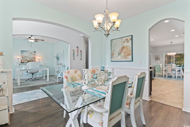 dining room featuring a chandelier, dark wood-style floors, arched walkways, ceiling fan, and a wainscoted wall