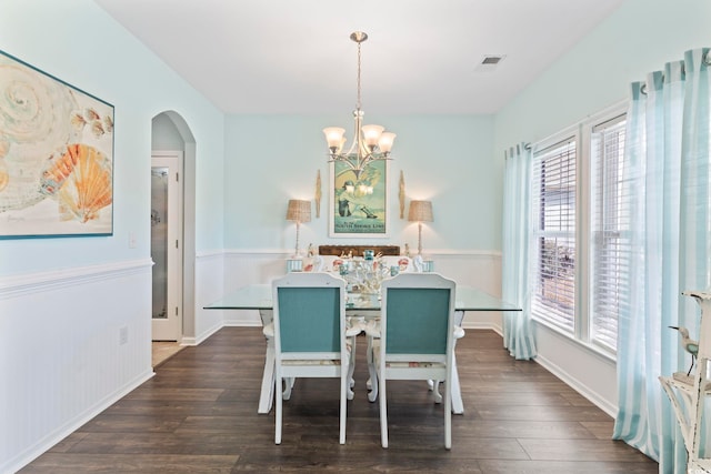dining room featuring dark wood-type flooring, a chandelier, arched walkways, and baseboards