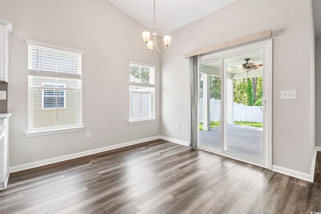 unfurnished dining area featuring dark wood-style floors, lofted ceiling, a chandelier, baseboards, and ceiling fan