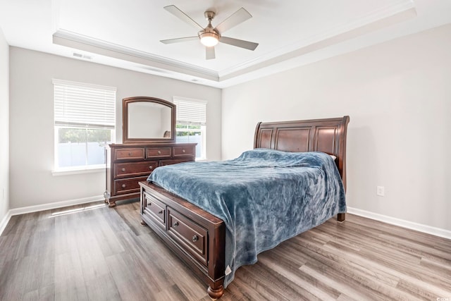 bedroom featuring a tray ceiling, wood finished floors, crown molding, and baseboards