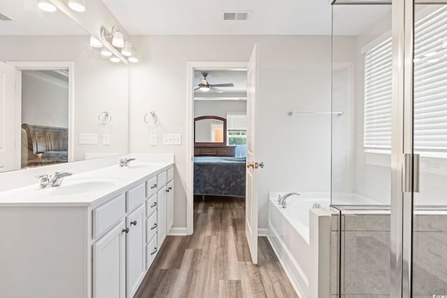 ensuite bathroom with wood finished floors, a ceiling fan, a bath, double vanity, and baseboards