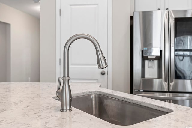 kitchen view of stainless steel refrigerator with ice dispenser, a sink, light stone countertops, and white cabinetry