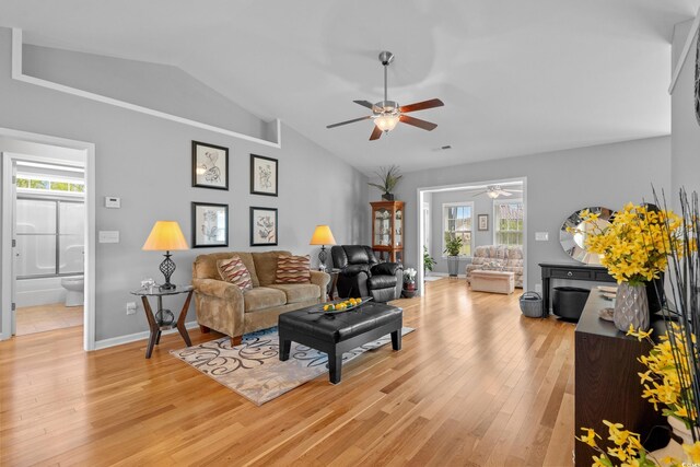living area featuring a ceiling fan, lofted ceiling, light wood finished floors, healthy amount of natural light, and baseboards