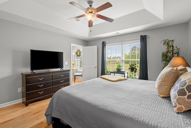 bedroom featuring a raised ceiling, light wood-type flooring, baseboards, and ceiling fan