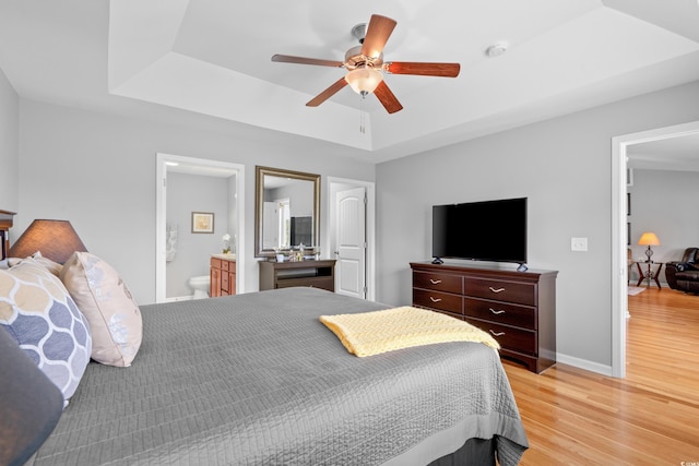 bedroom featuring a tray ceiling, light wood finished floors, baseboards, connected bathroom, and a ceiling fan