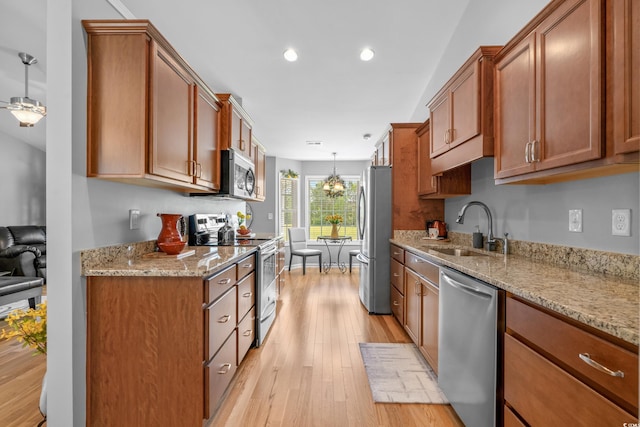 kitchen featuring stainless steel appliances, a sink, light wood-style flooring, light stone counters, and brown cabinetry