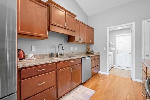 kitchen featuring appliances with stainless steel finishes, a sink, light wood finished floors, vaulted ceiling, and brown cabinets