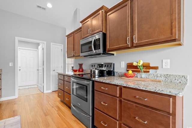 kitchen with stainless steel appliances, light wood-type flooring, light stone countertops, brown cabinetry, and baseboards