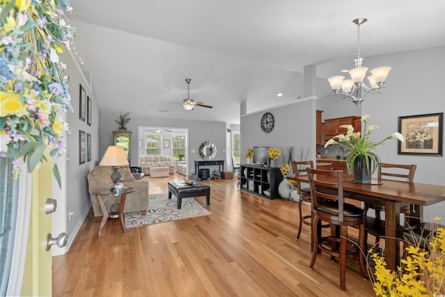 dining room featuring light wood-type flooring, a chandelier, ceiling fan, vaulted ceiling, and baseboards