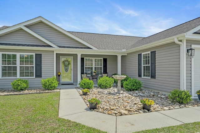 view of front of property with roof with shingles, a garage, a front lawn, and a porch