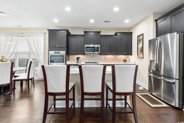 1681 Suncrest Dr, Myrtle Beach, SC 29577 - kitchen with stainless steel appliances, a kitchen island with sink, decorative backsplash, dark wood-style flooring, and light countertops