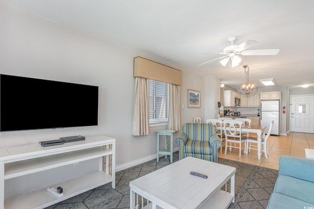 living room featuring a ceiling fan, healthy amount of natural light, baseboards, and a chandelier