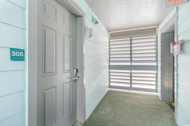 hallway featuring carpet flooring and wood walls