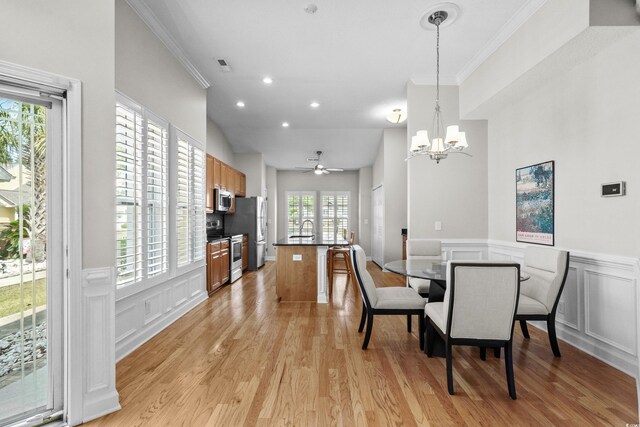 dining area with a chandelier, crown molding, light wood finished floors, a decorative wall, and a ceiling fan