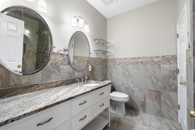 bathroom featuring tile walls, a shower stall, toilet, vanity, and wainscoting