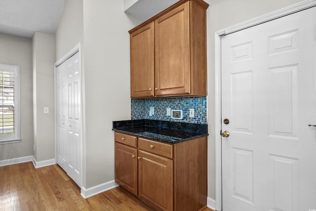 kitchen with light wood-style flooring, dark stone countertops, tasteful backsplash, and brown cabinetry