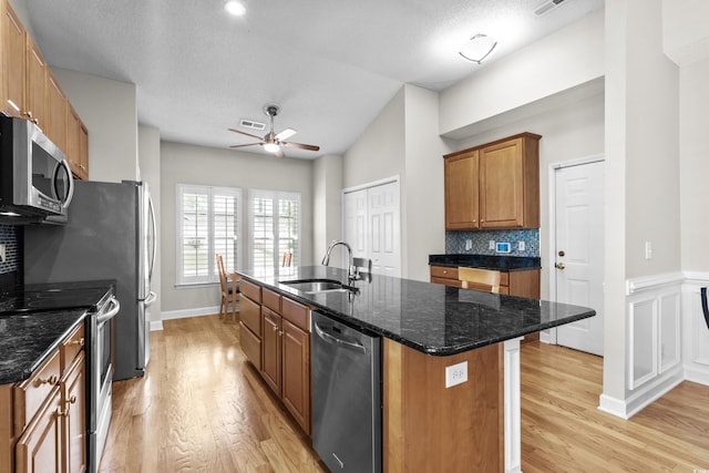 kitchen with a sink, stainless steel appliances, light wood finished floors, ceiling fan, and vaulted ceiling