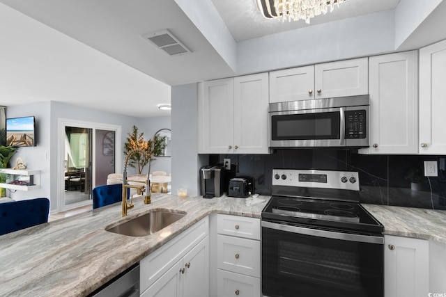 kitchen with stainless steel appliances, white cabinetry, backsplash, a sink, and light stone countertops