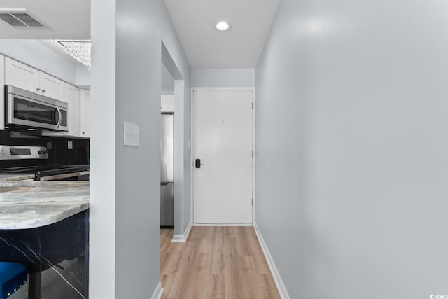 hallway featuring light wood-style flooring, baseboards, and recessed lighting