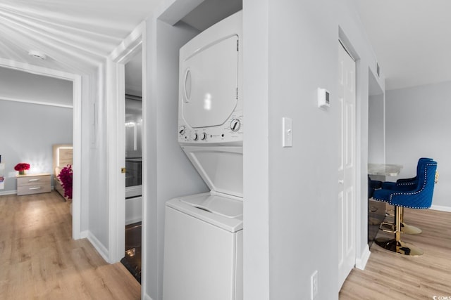 clothes washing area featuring stacked washer / drying machine, light wood-style floors, and baseboards