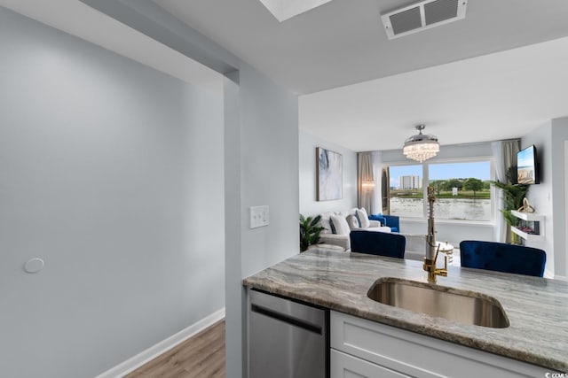 kitchen with stainless steel dishwasher, a sink, light stone countertops, light wood-style flooring, and white cabinets