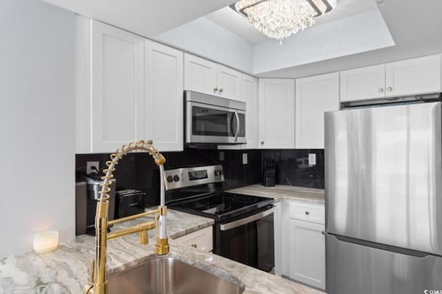 kitchen with stainless steel appliances, white cabinetry, light stone counters, backsplash, and a sink