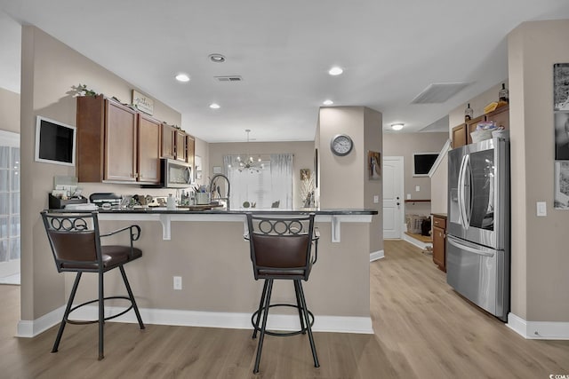9232 Goodwill Ct, Myrtle Beach, SC 29579 - kitchen with appliances with stainless steel finishes, a peninsula, light wood finished floors, a breakfast bar, and brown cabinets