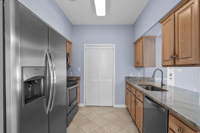 kitchen featuring appliances with stainless steel finishes, a sink, light stone counters, light tile patterned floors, and baseboards