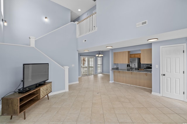 unfurnished living room with a chandelier, a high ceiling, light tile patterned flooring, baseboards, and a sink