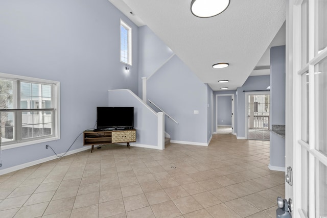unfurnished living room featuring light tile patterned floors, a textured ceiling, baseboards, stairs, and a high ceiling