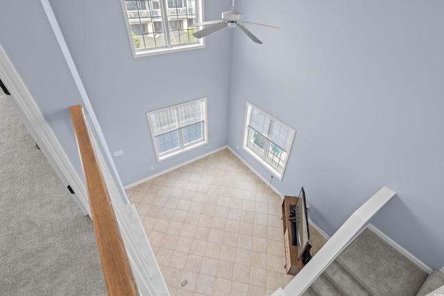 staircase with plenty of natural light, ceiling fan, a towering ceiling, carpet, and baseboards