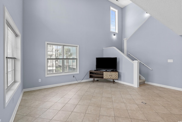 unfurnished room with a high ceiling, stairway, light tile patterned flooring, and baseboards