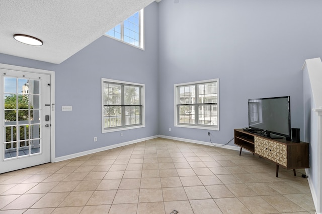 unfurnished living room with healthy amount of natural light, a towering ceiling, light tile patterned floors, baseboards, and a textured ceiling
