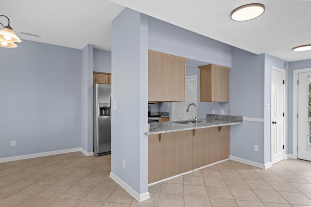 kitchen featuring stainless steel fridge with ice dispenser, a sink, light brown cabinetry, a breakfast bar area, and light tile patterned floors