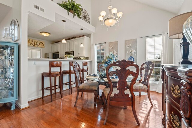 dining area featuring a chandelier, high vaulted ceiling, wood finished floors, and baseboards