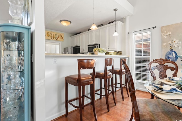 kitchen with stainless steel appliances, light wood-style floors, a breakfast bar area, white cabinetry, and hanging light fixtures