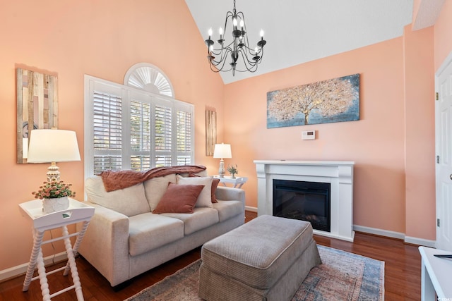 living room with a chandelier, high vaulted ceiling, wood finished floors, baseboards, and a glass covered fireplace